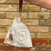 Beige geometric patterned pouch with a tassel held against a brick wall.