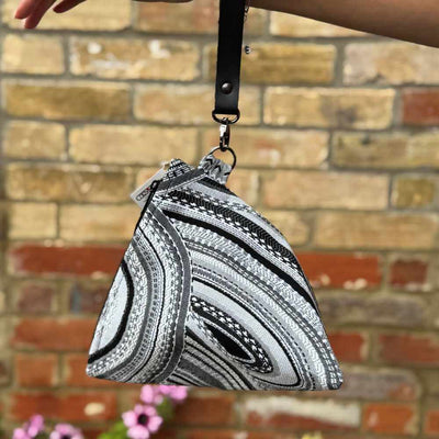 Black and white patterned bag held by a hand against a brick wall.