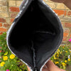 Black pouch with silver zipper held in front of a brick wall and garden.
