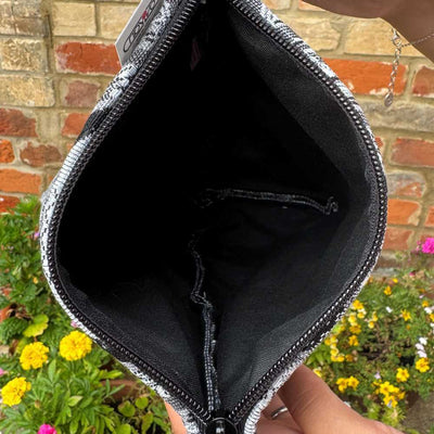 Black pouch with silver zipper held in front of a brick wall and garden.