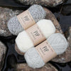 Three skeins of yarn with 'PIP Naturals' labels on rocks by a body of water | Yarn Worx