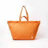 An orange canvas tote bag with dual top handles and a small white brand tag on the lower right corner, photographed against a clean white background | Yarn Worx