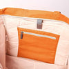 Close-up of the interior of a tote bag showing a quilted cream lining, an orange zippered pocket, and orange fabric trim with a gray zipper pull | Yarn Worx
