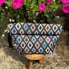 Patterned roll top bag on a wooden stool with pink flowers in the background