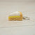 Keychain shaped like a slice of cake with white frosting and yellow filling on a light wooden surface.