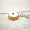 Donut-shaped keychain with white icing and a red berry on a light wooden surface.