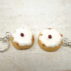 Two small keychain charms shaped like donuts with white icing and a red berry on a light wooden surface.