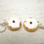 Two small keychain charms shaped like donuts with white icing and a red berry on a light wooden surface.