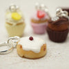 Close-up of a keychain shaped like a small cake with white frosting and a red cherry on top, with other similar keychains in the background.