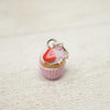 Cupcake charm with a red cherry on top on a textured beige surface