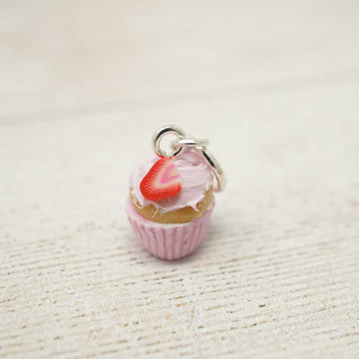 Cupcake charm with a red cherry on top on a textured beige surface