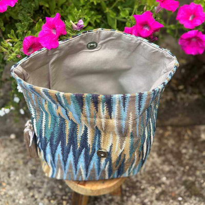 Multicolored patterned bag with a gray interior against a background of pink flowers.