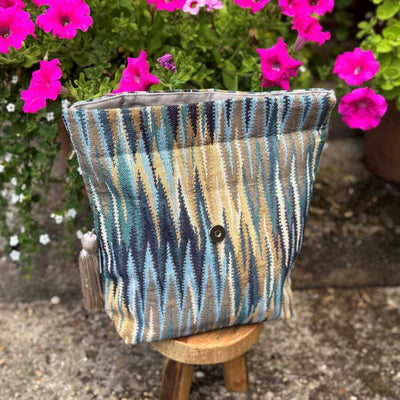 Textured fabric project bag with a button on a small wooden stool, surrounded by pink flowers.