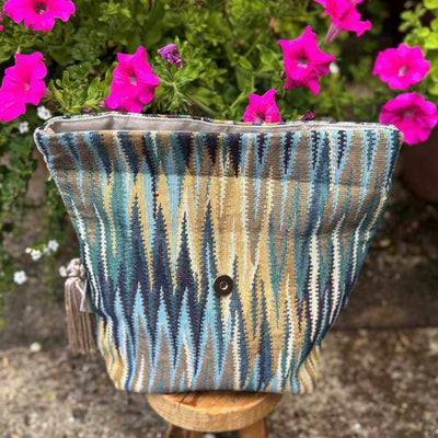 Striped fabric project bag with tassels in front of pink flowers